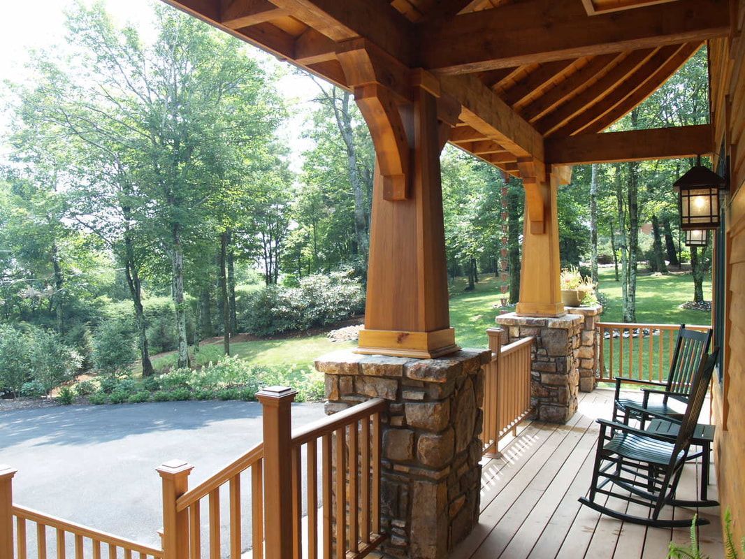 Covered wooden porch with stone columns, rocking chair, and view of a tree-lined road and grassy yard