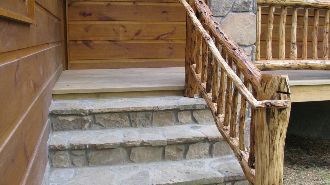 Stone steps beside a rustic wooden railing leading to a cabin-style doorway