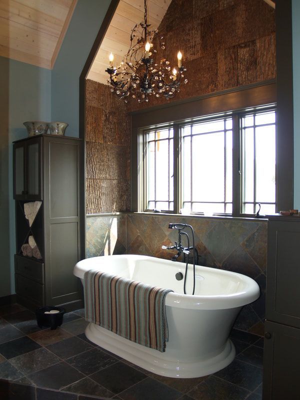 Elegant bathroom with freestanding white bathtub, chandelier, and large window with wood-paneled walls.