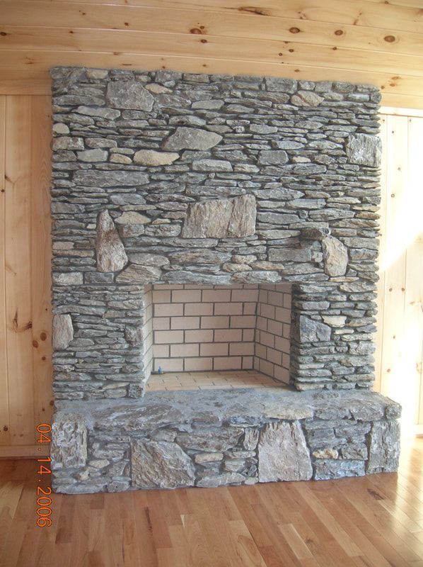Stone fireplace set into a wood-paneled room with a brick firebox and hardwood floor