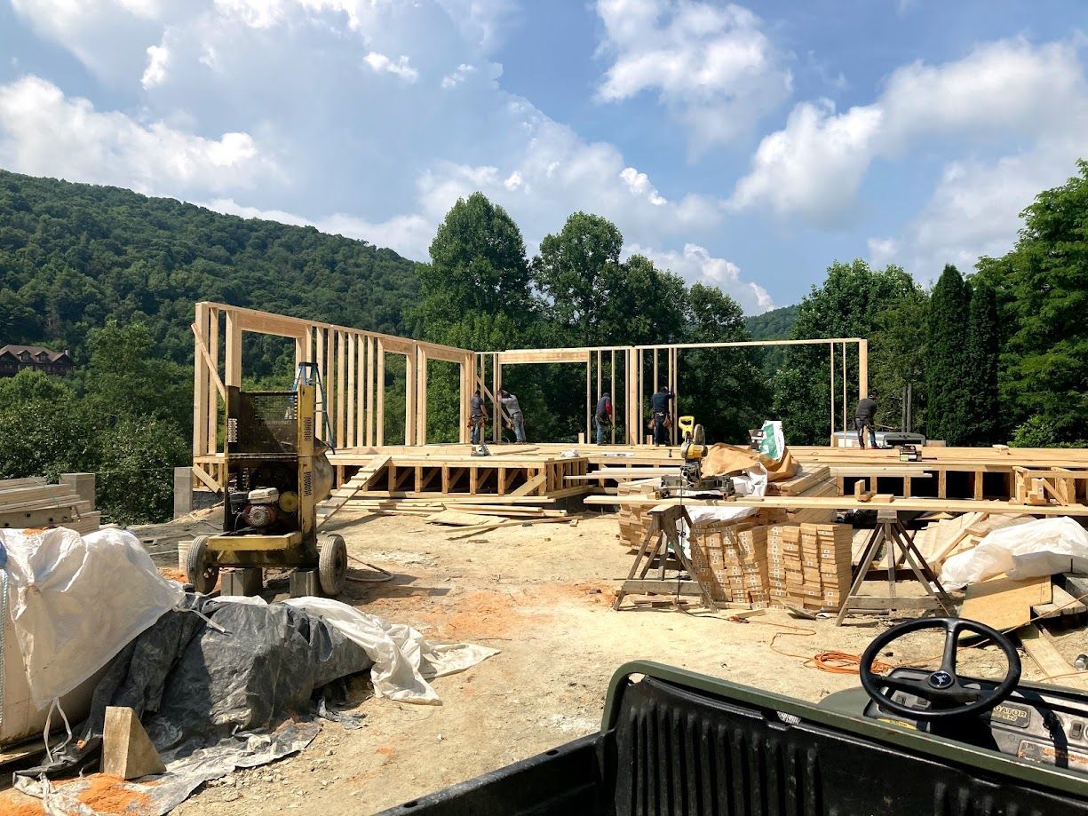 Wooden house frame under construction on a rocky site with forested hills in the background
