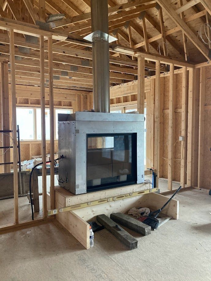 Unfinished room with exposed framing and a central wood-burning stove on a raised hearth.