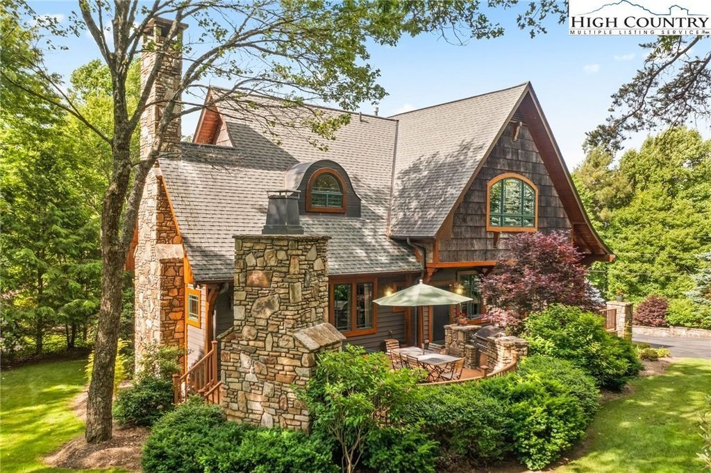 Stone cottage with a steep roof, lush garden, and patio umbrella in a sunny yard
