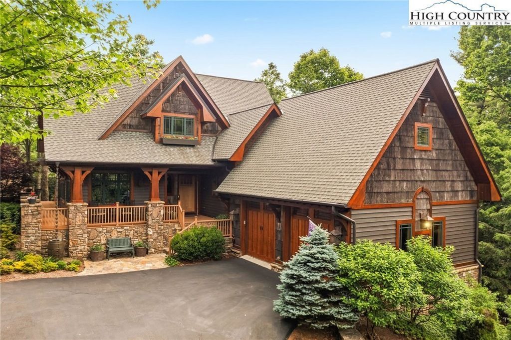 Wooden mountain-style house with stone accents, steep roof, and landscaped driveway surrounded by trees