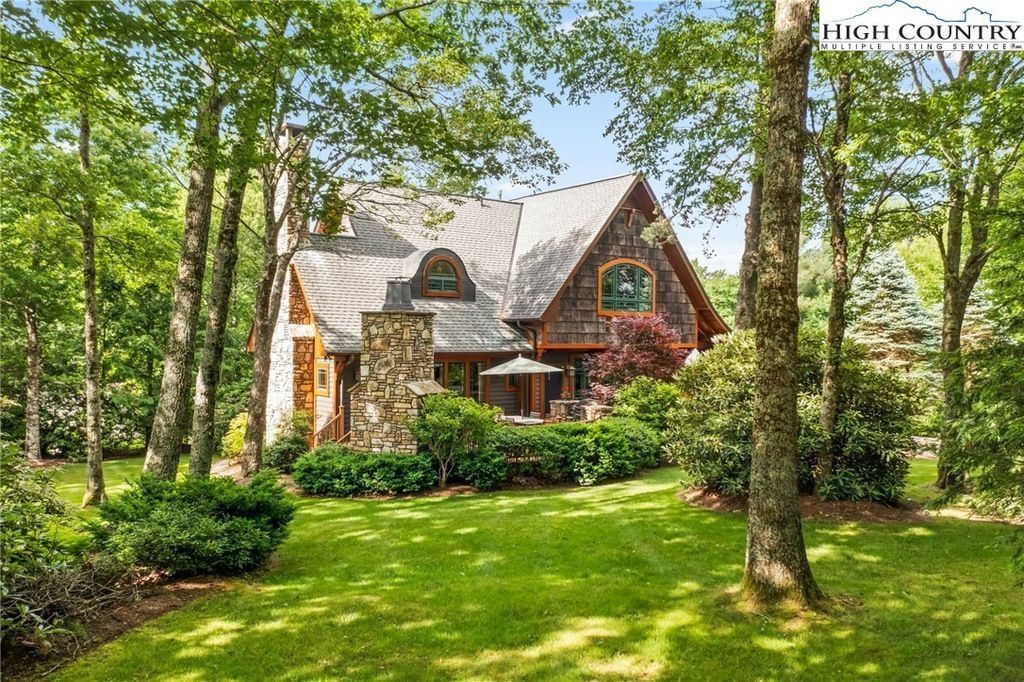 Stone house with a steep roof surrounded by tall trees and a lush green lawn