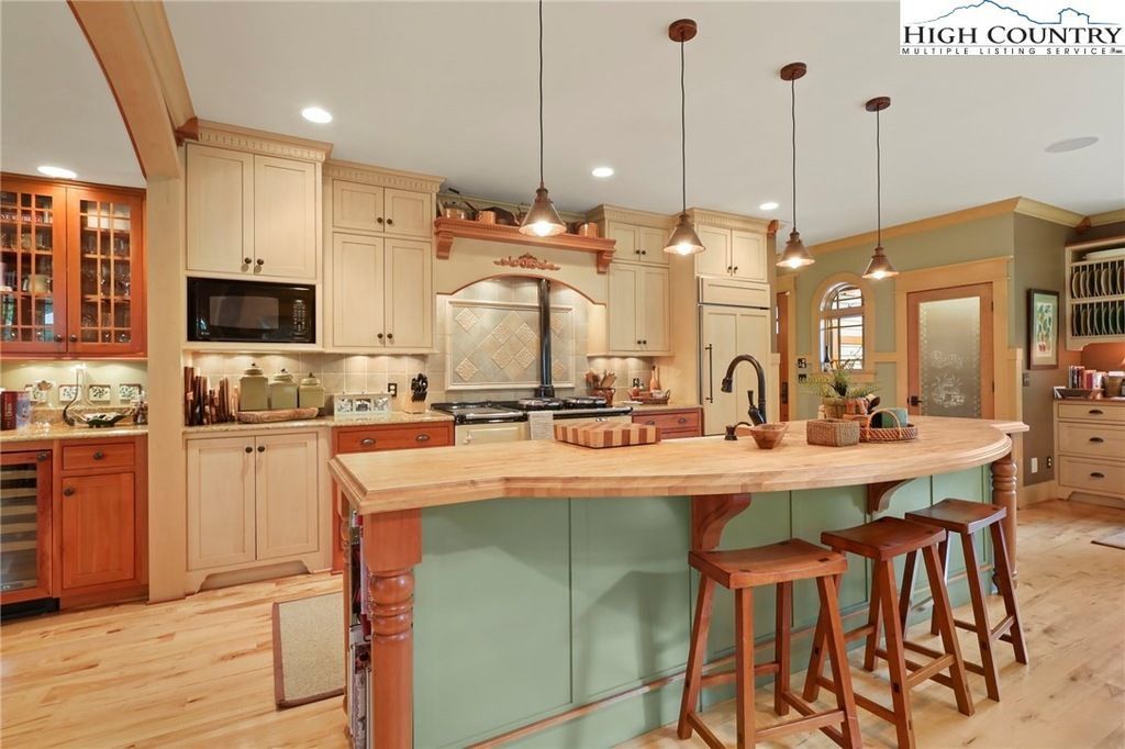 Bright kitchen with mint island, wood stools, cream cabinets, and pendant lights