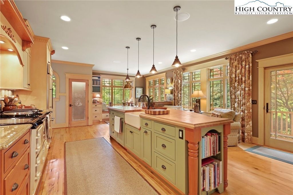 Bright gourmet kitchen with island, hanging lights, wood floors, and large windows overlooking trees
