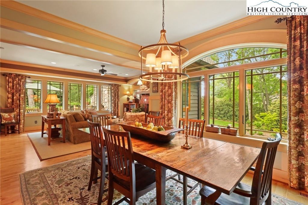 Elegant dining room with large windows, wooden table, chandelier, and lush outdoor view
