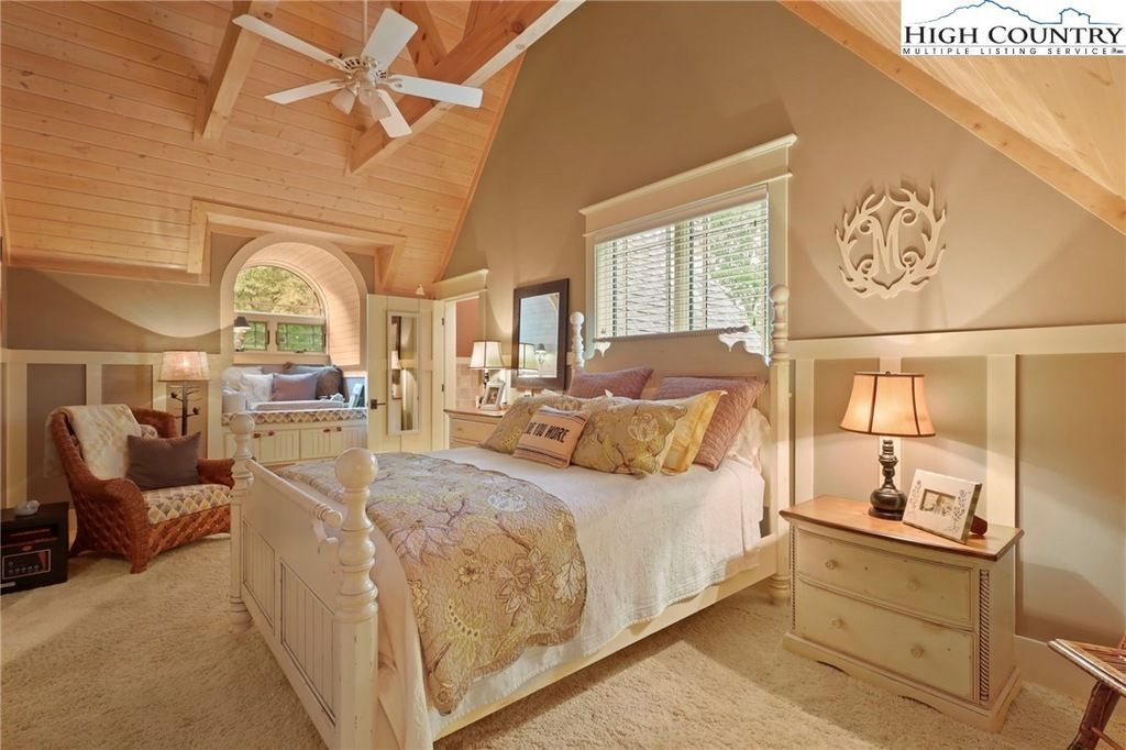 Cozy beige bedroom with a white bed, ceiling fan, bedside table, and large window.