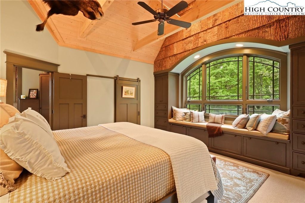 Cozy bedroom with vaulted wood ceiling, large arched window seat, and neutral bedding