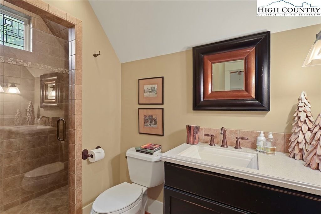 Bathroom vanity with mirror, sink, toilet, and glass shower door in warm tan tones