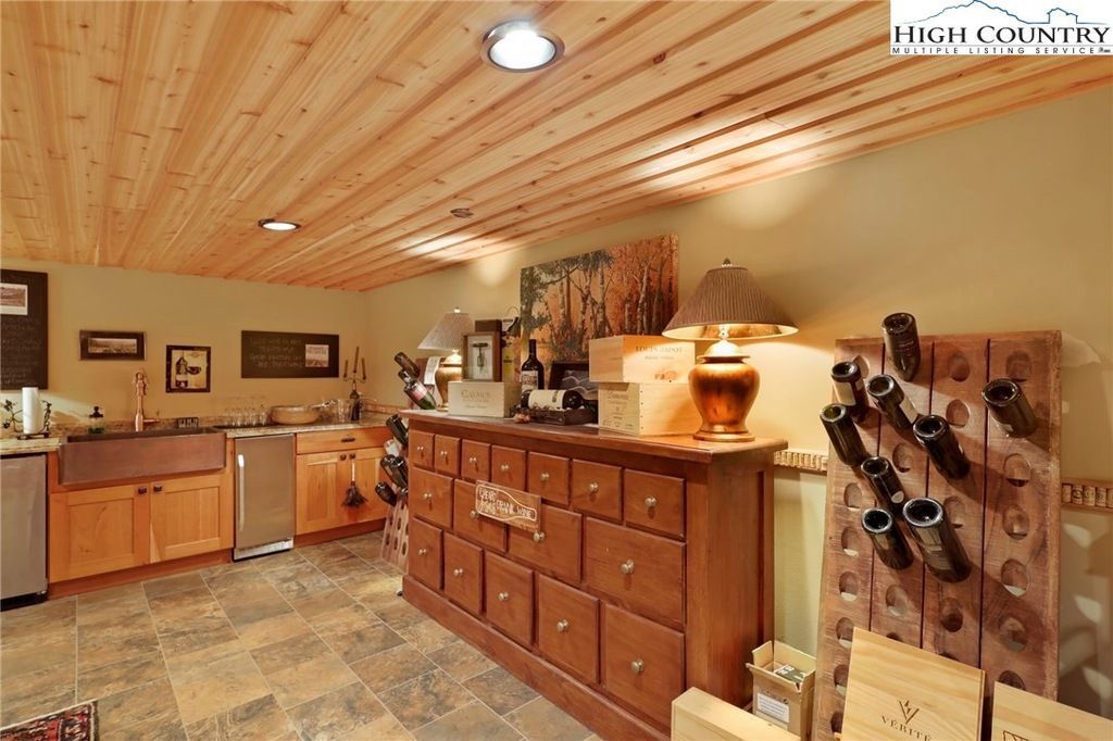 Rustic kitchen with wood cabinets, stone floor, and wine rack under a slatted wood ceiling