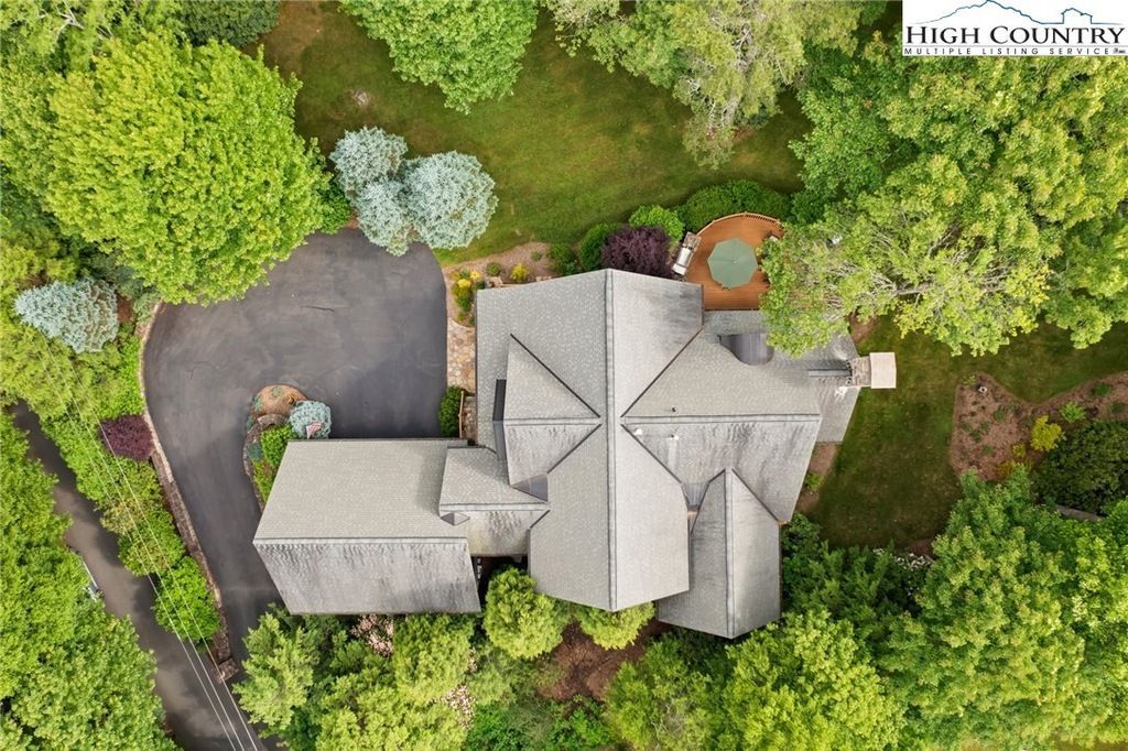 Aerial view of a house with gray roof, driveway, and lush green trees surrounding the property.