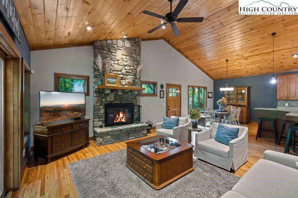 Spacious rustic living room with stone fireplace, wood ceiling, and gray sofas around a coffee table
