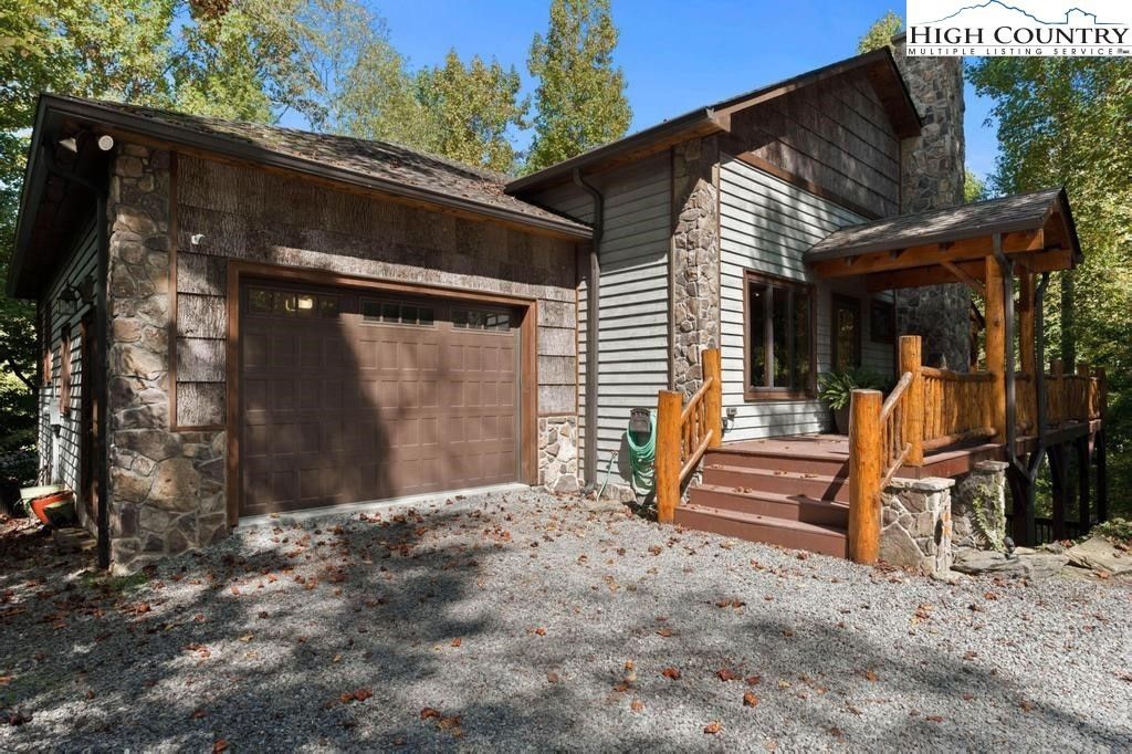 Rustic house exterior with a double garage, front porch, and gravel driveway surrounded by trees