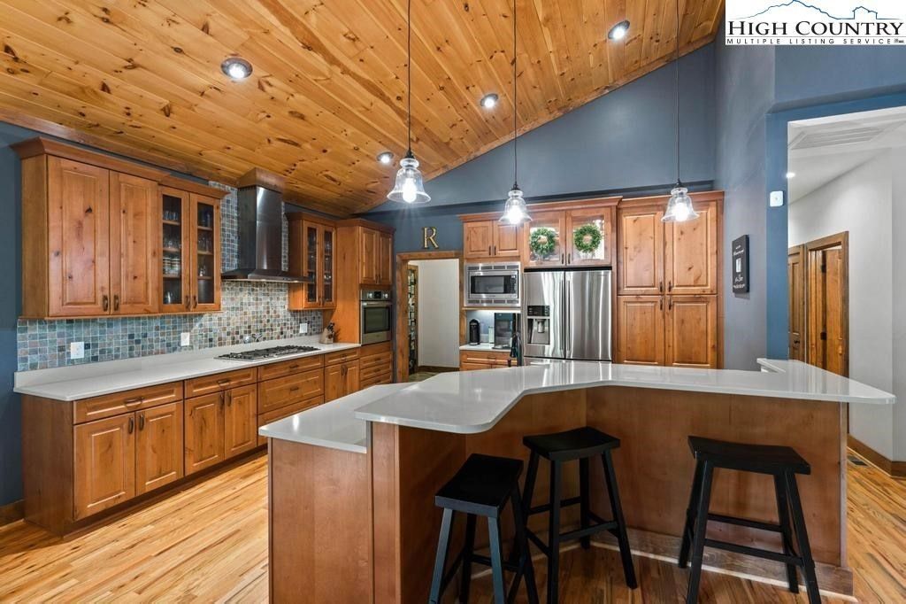 Spacious rustic kitchen with wood ceiling, island, stainless steel appliances, and bar stools.
