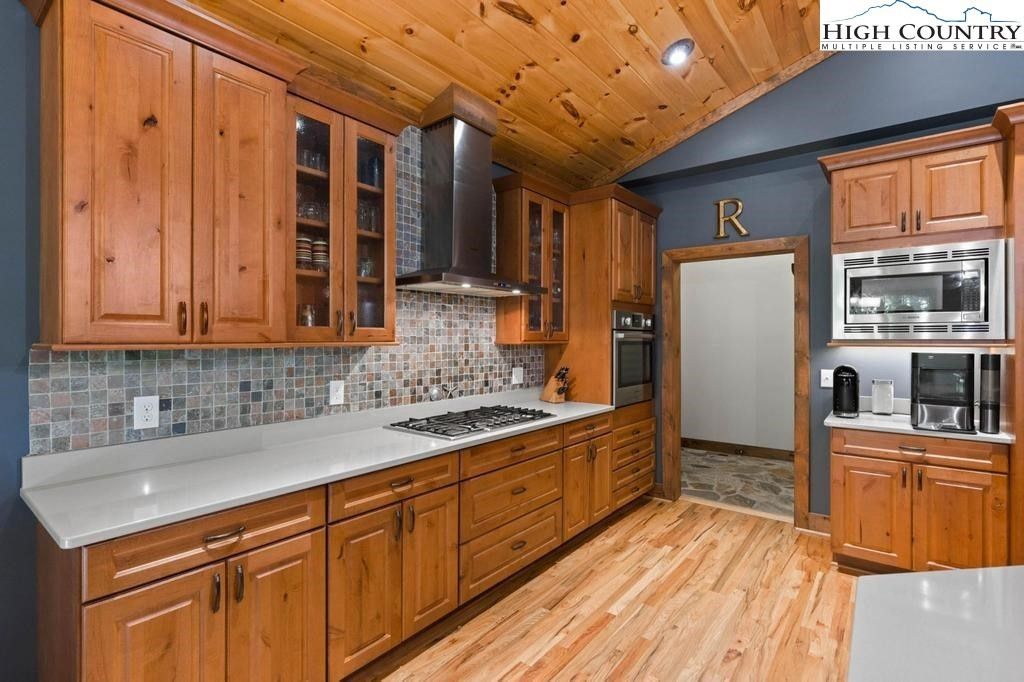 Wood-paneled kitchen with wooden cabinets, white countertops, stainless appliances, and hardwood floor.