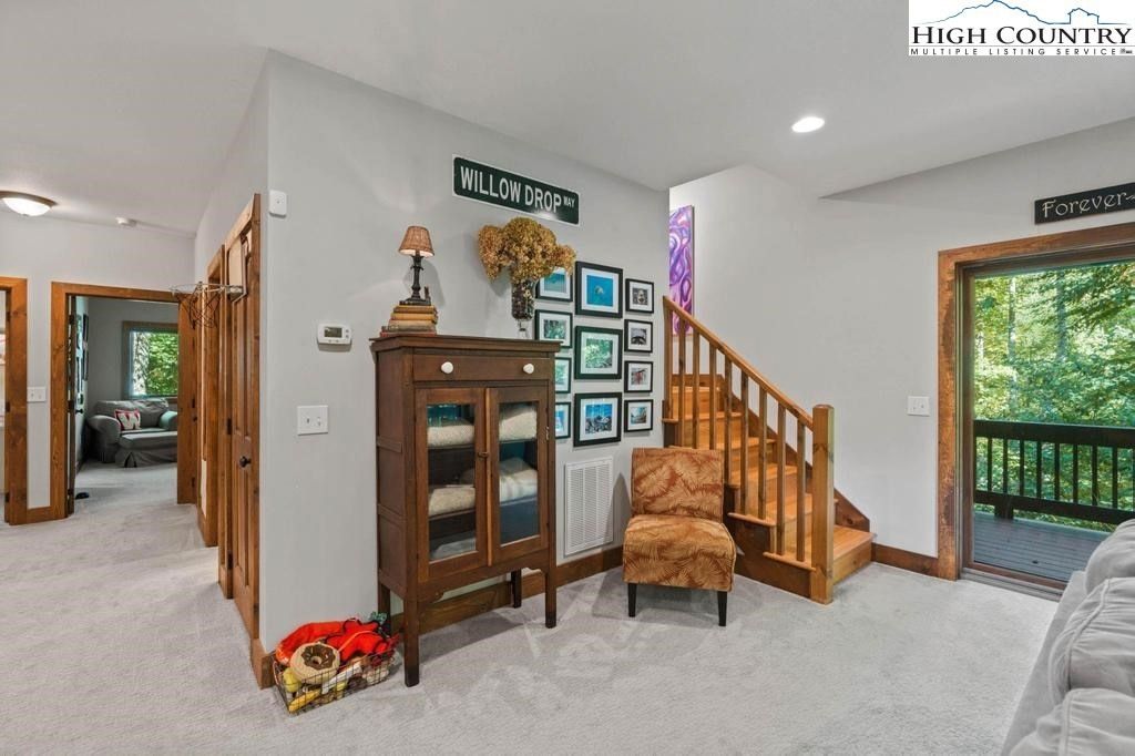 Bright living room with wood stair railing, glass cabinet, framed art, and sliding door to a deck
