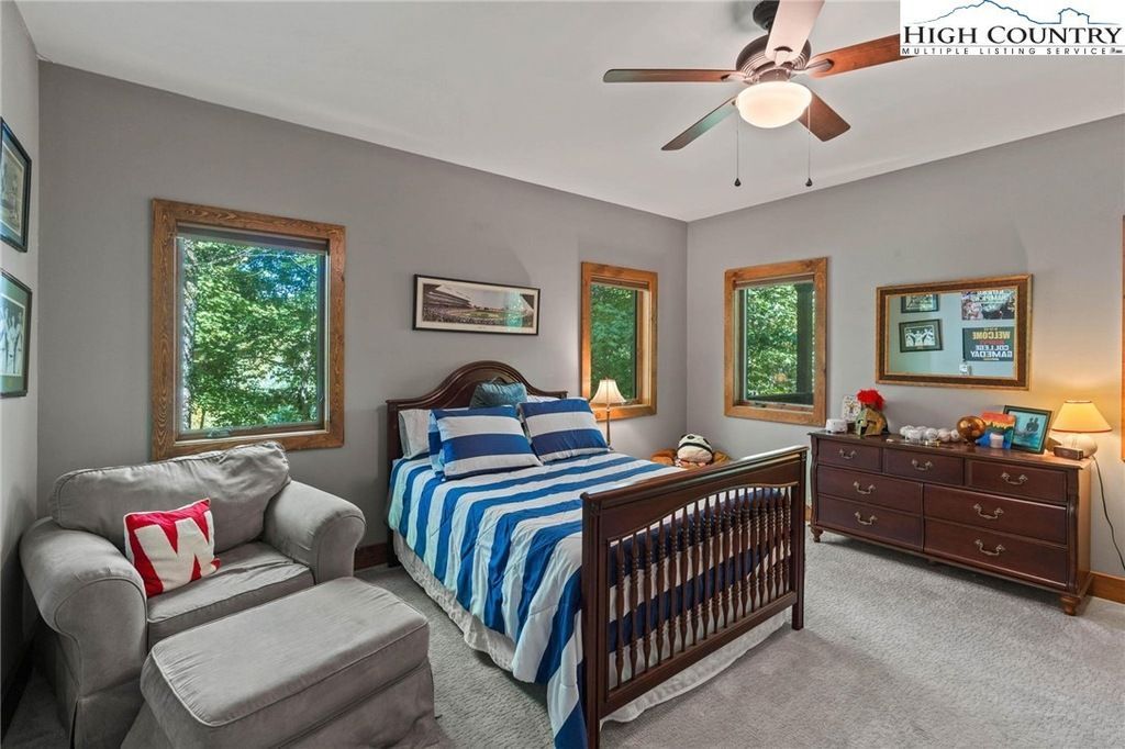 Bright bedroom with gray walls, striped blue bedspread, wooden dresser, and large windows.