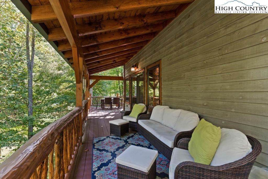 Covered wooden porch with wicker seating, patterned rug, and green cushions overlooking trees