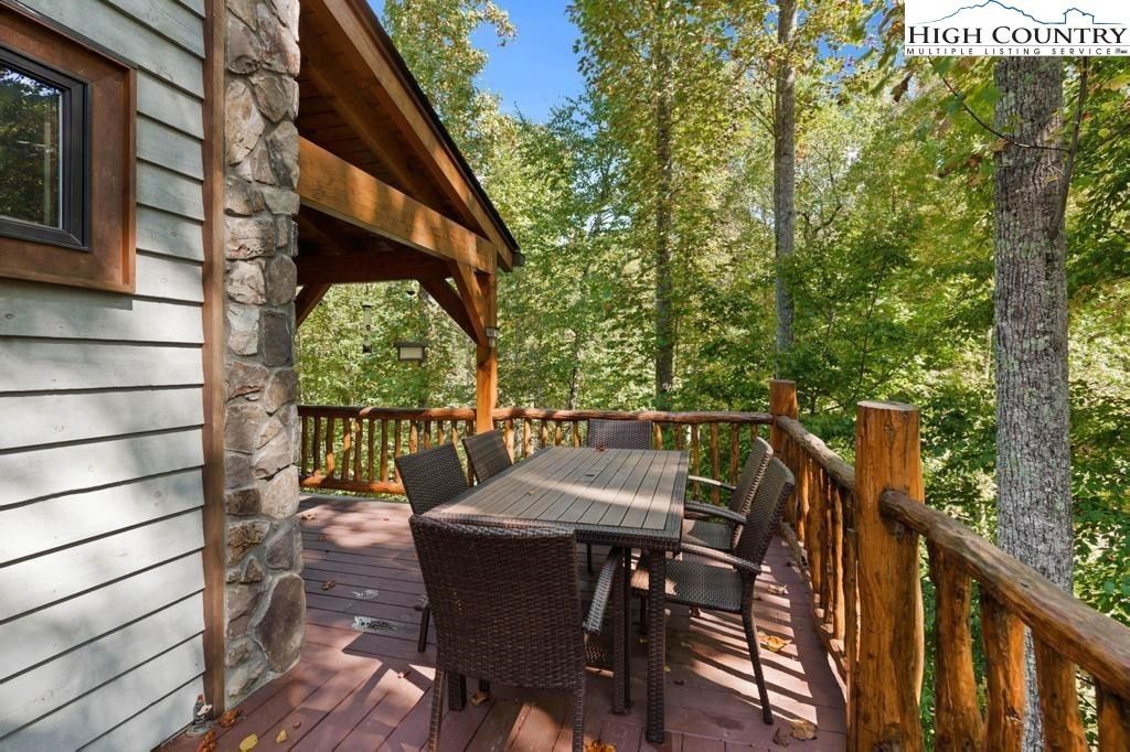 Wooden deck with outdoor dining table and chairs beside a cabin, overlooking a wooded area.