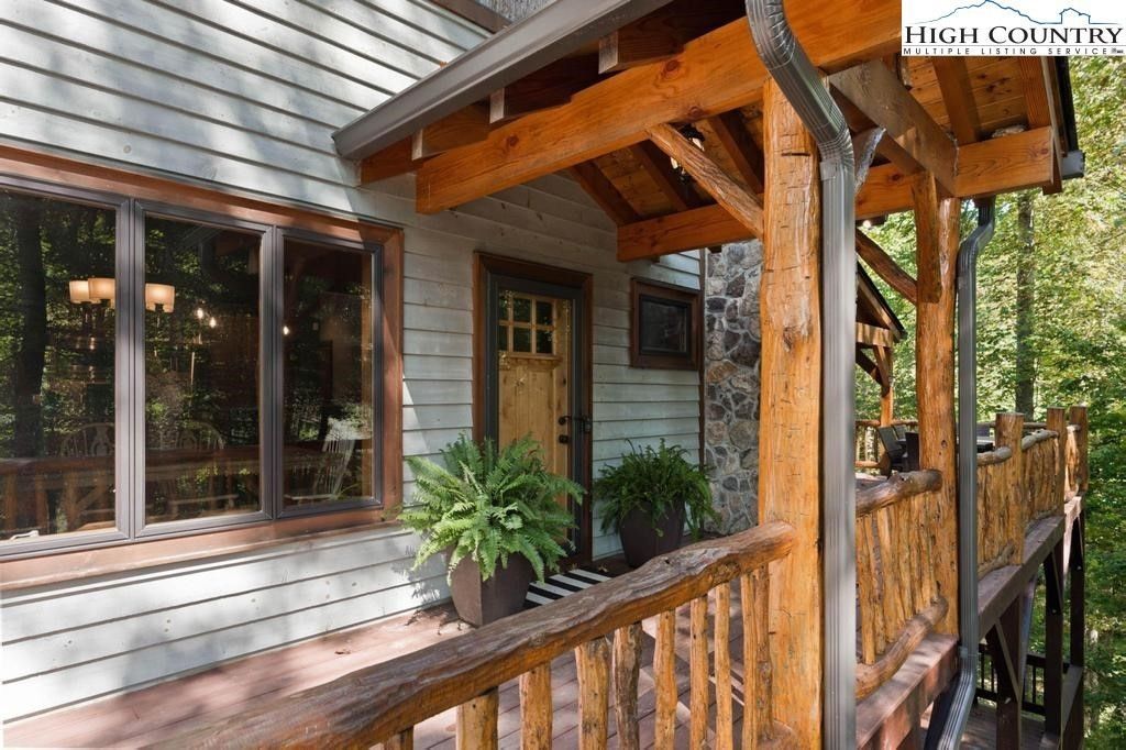 Wooden porch with railing and potted plants beside large windows on a rustic house