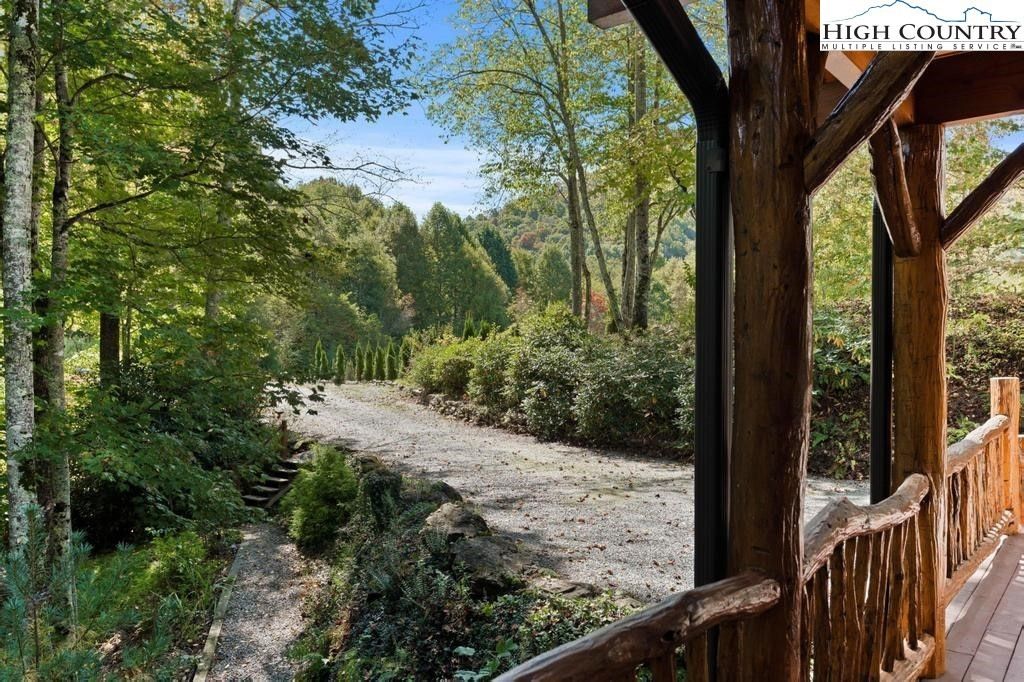 Wooden porch overlooking a sunlit gravel path lined with green trees and shrubs