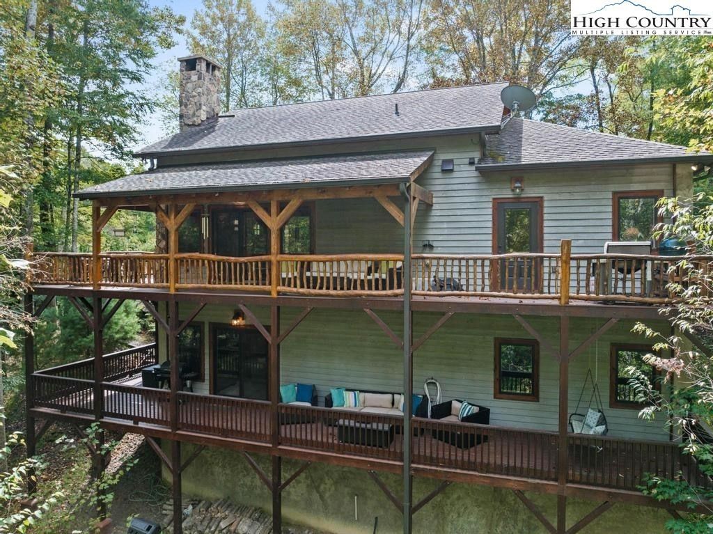 Two-story log cabin with wraparound porches surrounded by trees in a wooded setting