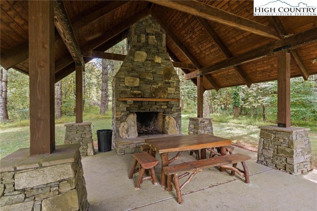 Covered picnic shelter with a stone fireplace, wooden table, and benches in a wooded park area