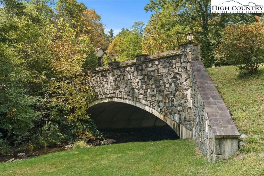 Stone arch bridge over a grassy path in a park with trees and autumn foliage.