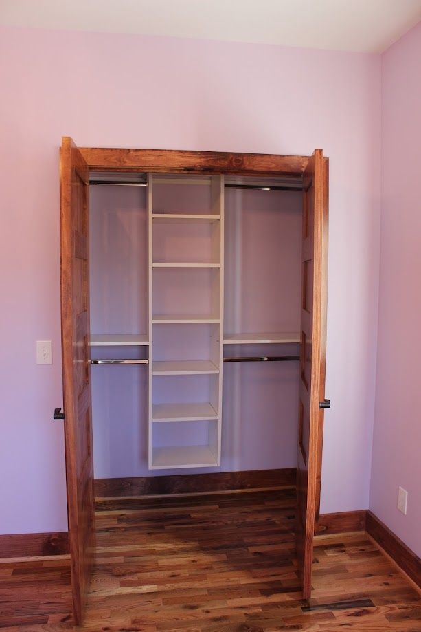 Empty walk-in closet with lavender walls and wood flooring, featuring a hanging organizer and shelves.