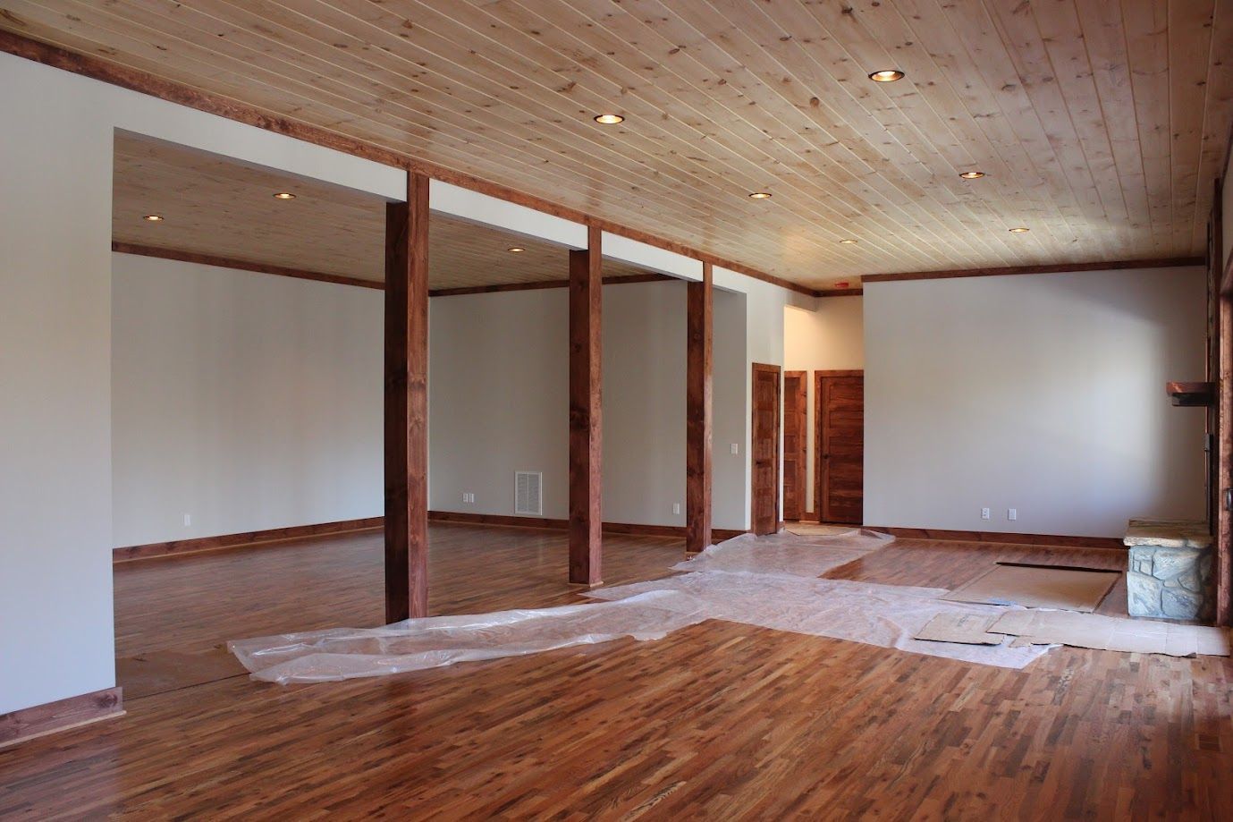 Empty room with wood floors, exposed beams, and white walls under renovation