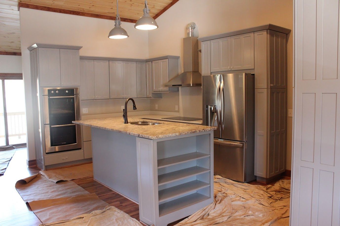 Modern kitchen with gray cabinets, stainless steel appliances, marble island, and pendant lights.