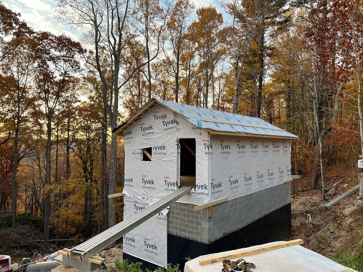 Partially built house wrapped in white housewrap, with a ramp, surrounded by autumn trees