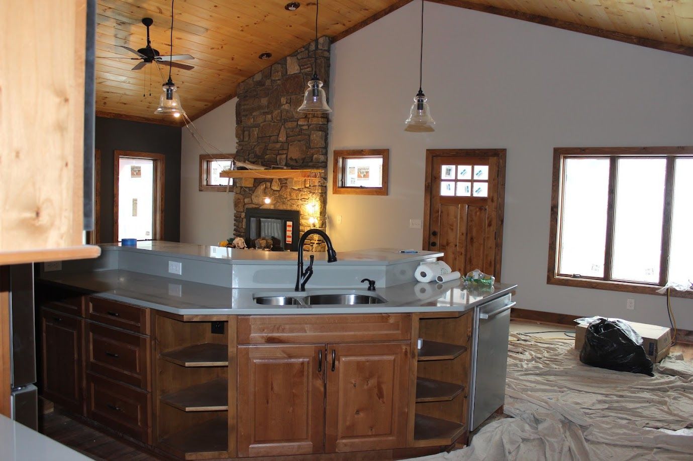 Rustic kitchen with stone fireplace, wood cabinets, island counter, and large windows