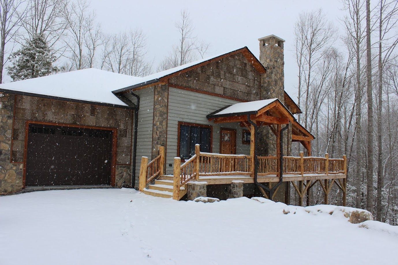 Snowy cabin with a dark garage and wooden porch in a winter forest