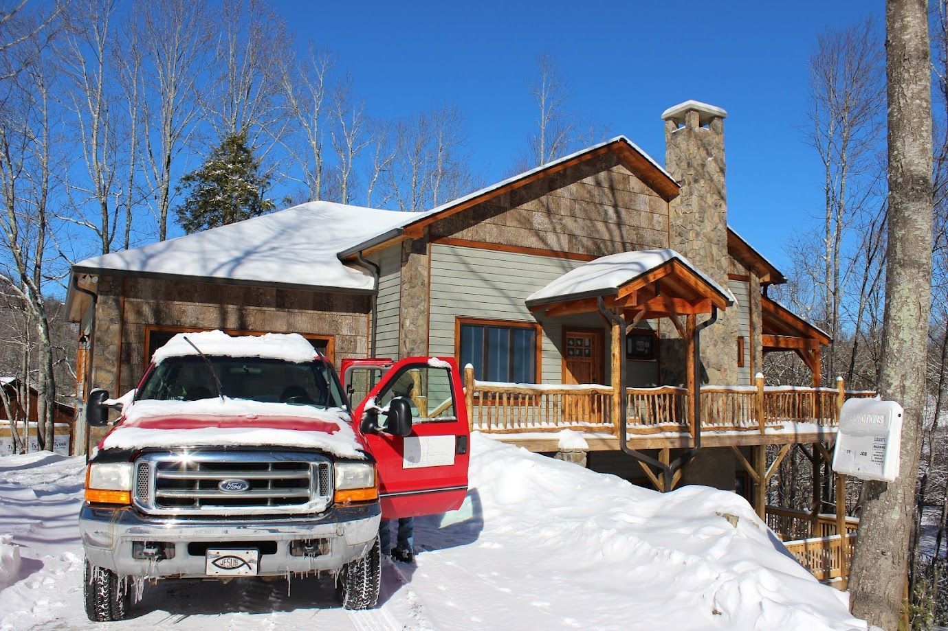 Snow-covered house with a red truck parked in front on a sunny winter day