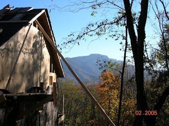 Mountain view behind a rustic wooden building and trees under a clear blue sky.