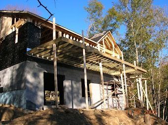 Partially built house with a covered porch and exposed roof framing on a wooded hillside