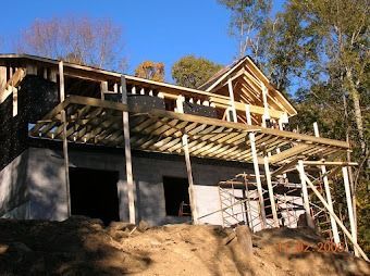 Partially built house with wooden framing and scaffolding on a dirt hillside under a blue sky