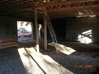 Interior of unfinished room with ladder, exposed beams, sunlight, and a workbench by the wall