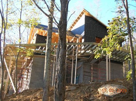 Partially built modern house with wooden framing, ladders, and scaffolding among trees