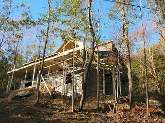Wooden house under construction on a wooded hillside with scaffolding and bare trees