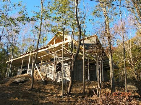 Partially built house on a wooded hillside with exposed framing and trees in front