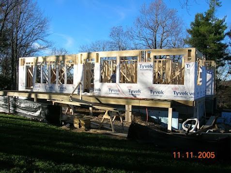 Partially built wooden house frame with Tyvek wrap, outdoors on a sunny day
