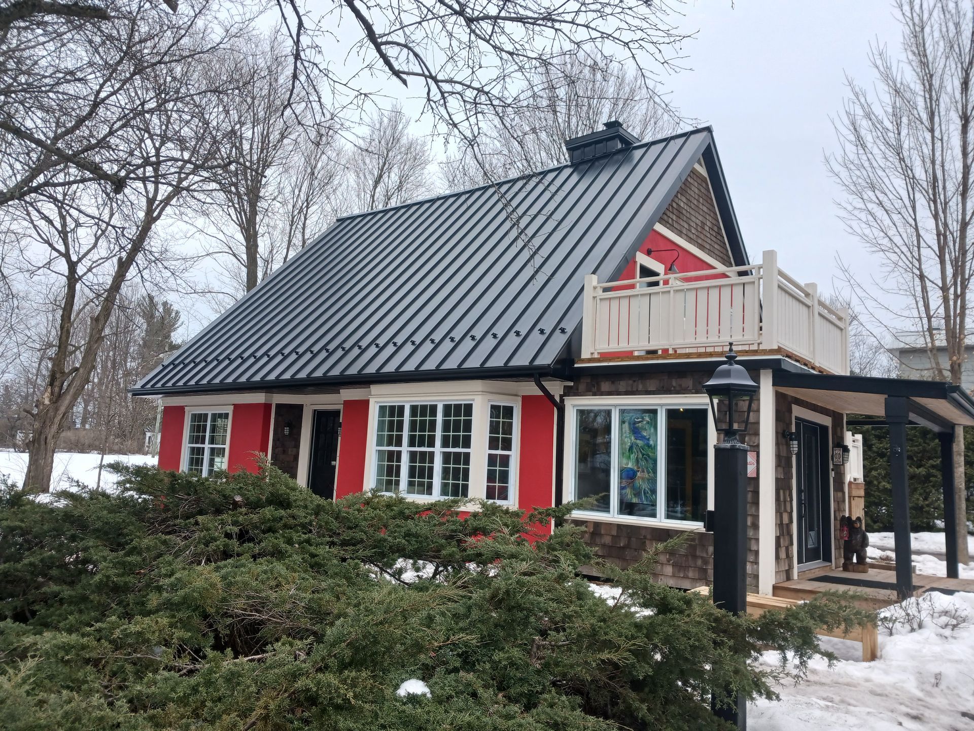 Une maison rouge avec un toit noir est entourée de neige et d'arbres.