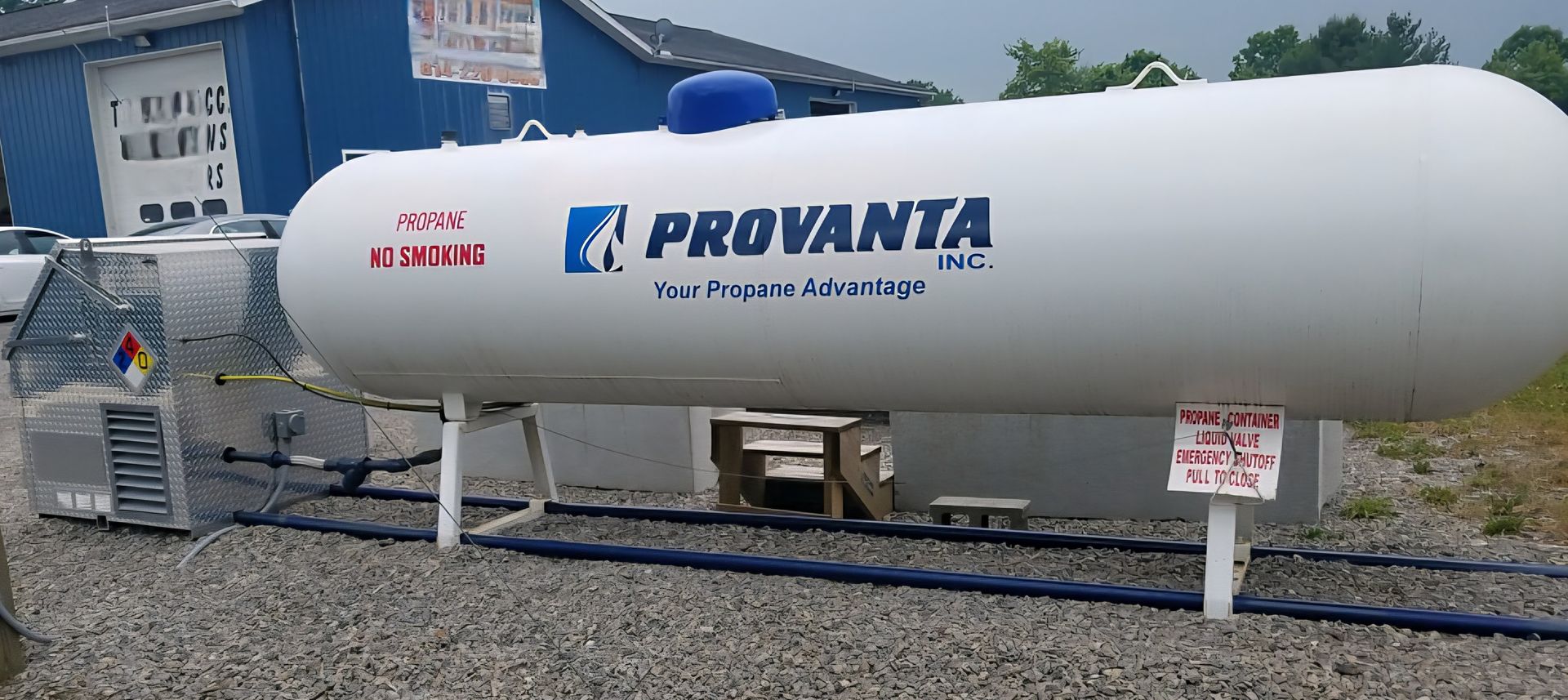 Three white propane trucks parked on a gravel lot with a wooded background. The trucks have the