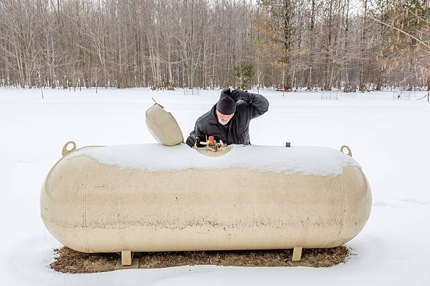 Man inspecting propane tank outdoors, wearing safety glasses and gloves.