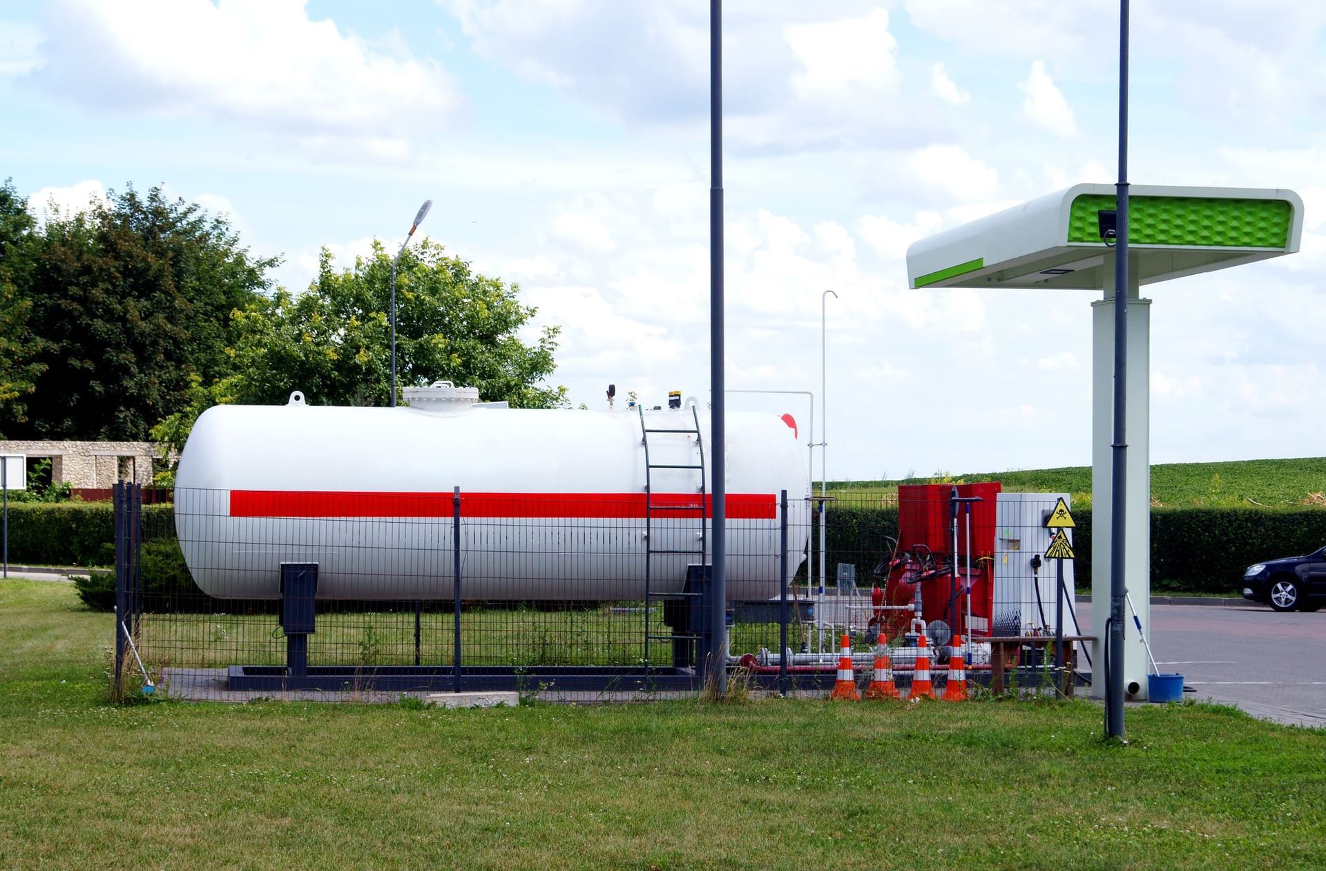 A gas tank is sitting in the grass next to a gas station.