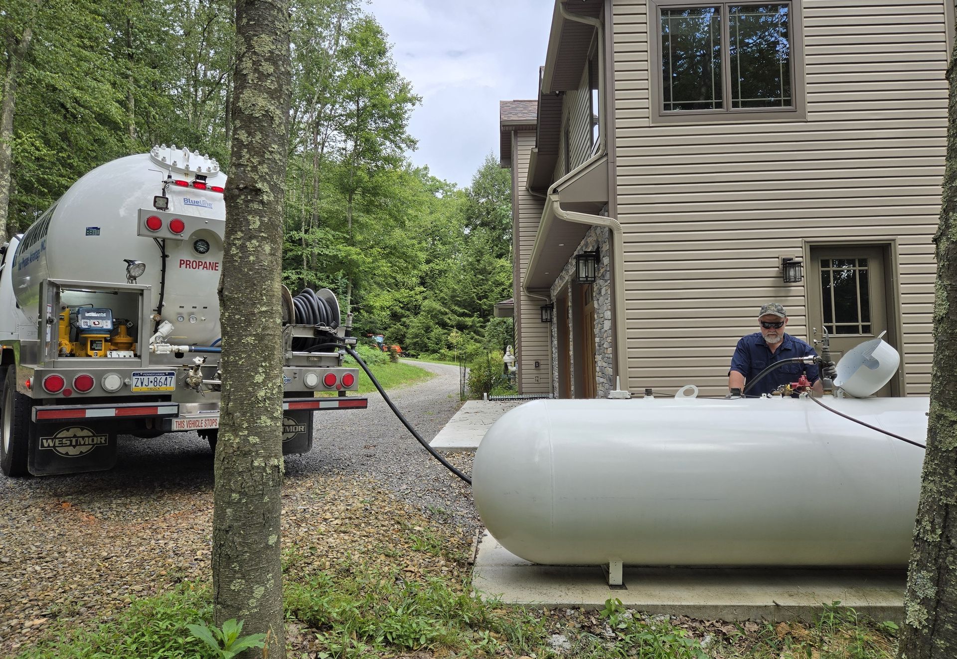 Propane truck refueling a large white tank next to a house; person working.